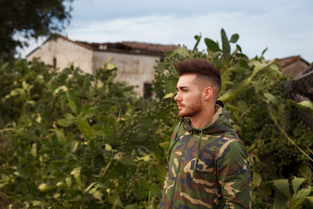 Attractive guy with military jacket and plants backgroundの写真素材