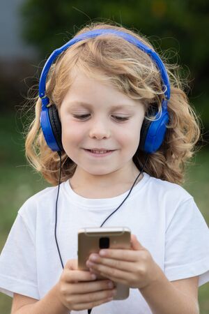 Funny child with long hair listening music with blue hadphones and a mobile in the parkの写真素材