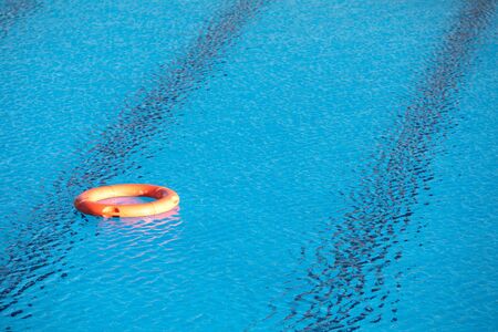 Orange lifebuoy floating on the surface of blue water in a pool