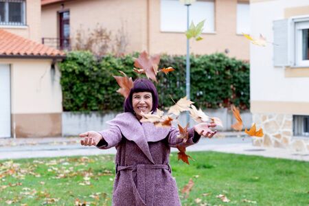 Happy woman with a purple coat throwing leaves in autumnの写真素材