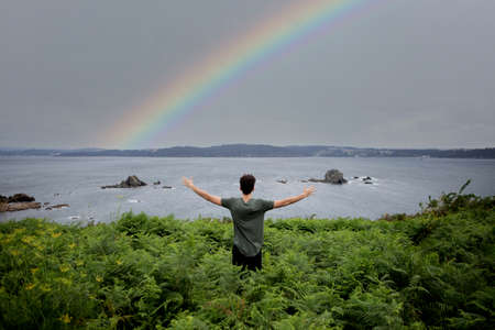 Happy guy with arms up enjoy freedom at the beach looking a beautiful rainbow
