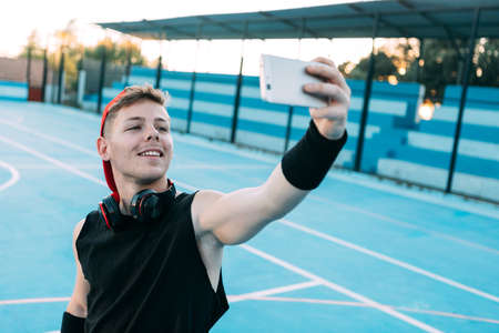 Attractive guy basketball player with a ball looks at his mobile phone and smiles while taking a breakの写真素材