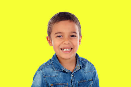 Latin child with denim shirt looking at camera and laughing isolated on a yellow backgroundの写真素材