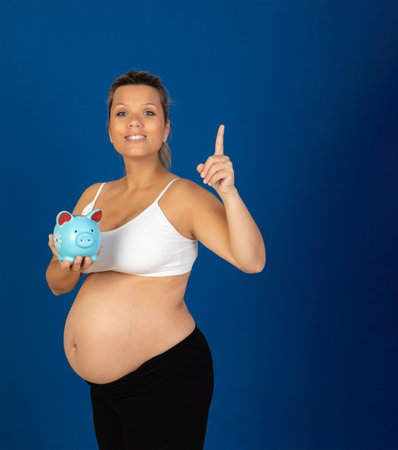 Pregnancy. Happy pregnant woman with a moneybox isolated on a blue backgroundの写真素材