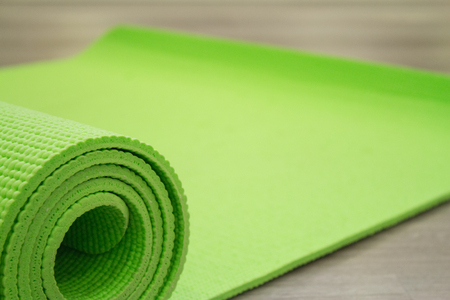 Green yoga mat unrolled on the wooden floor.の写真素材