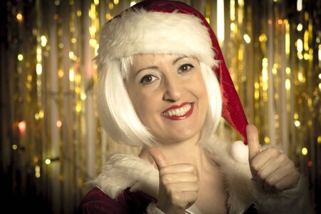 Portrait of woman disguised as Santa Claus. Positive attitude. She is smiling. Defocused gold background.の写真素材