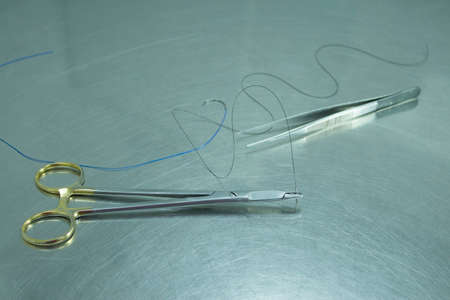 Scissors, tweezers and thread for stitches on metal table.の写真素材
