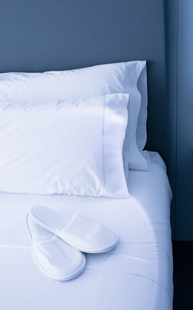 Bed sheets and white pillows and slippersの写真素材