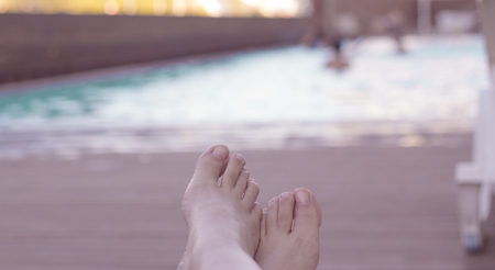 Relaxed atmosphere. Woman feet on chair at the pool.の写真素材