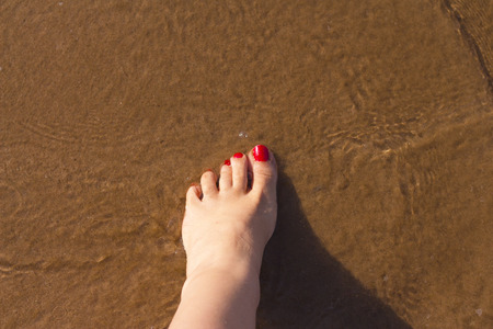 Beach scene with woman feet on the sand. Nails of feet painted redの写真素材
