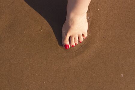 Beach scene with woman feet on the sand. Nails of feet painted red