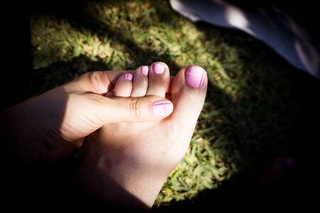 Foot and womans hand on the grass with pink painted nails