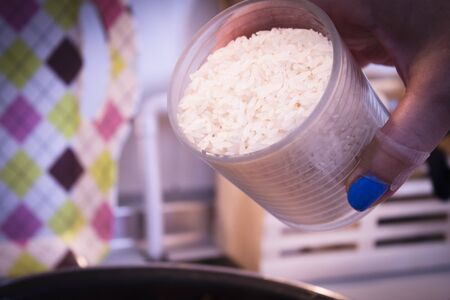 Glass cup with rice about to be thrown in the pan for paellaの写真素材