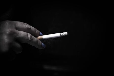 Womans hand holding lit cigarette. Dark backgroundの写真素材