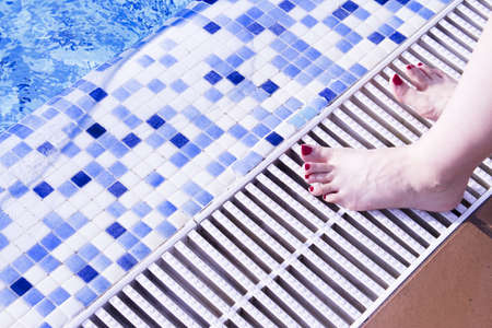 Bare feet of woman with nails painted red. Pool backgroundの写真素材