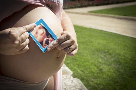 Seven month pregnant woman with ultrasound of baby on her gut. Pink dress colorの写真素材