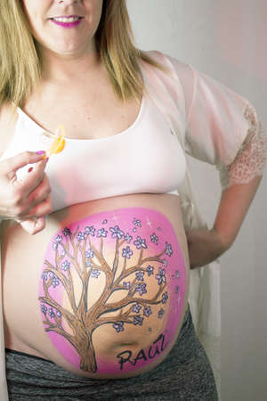 Eight month pregnant woman holding a pacifier in orange color
