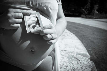 Seven month pregnant woman with ultrasound of baby on her gut. Pink dress color