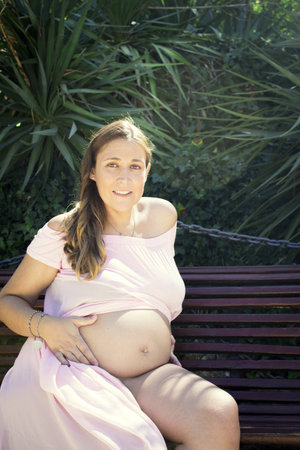 Seven months pregnant woman sitting on a wooden bench. Very happy expressionの写真素材