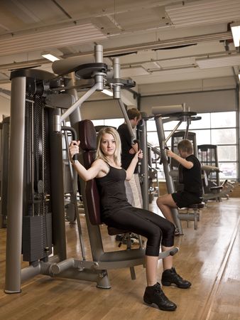 Girl using an exercise machine at a health club with two men in the background
