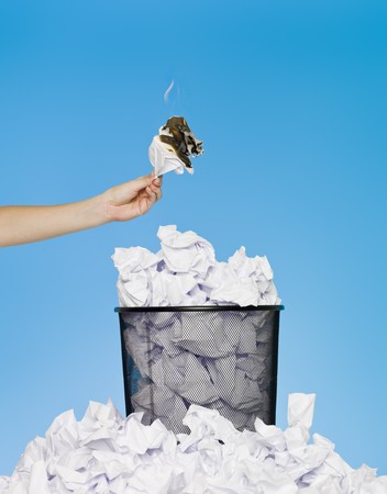 Hand holding a piece of paper in flames over a wastebasketの写真素材