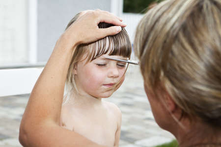 Woman cutting young girls hair outdoorの写真素材