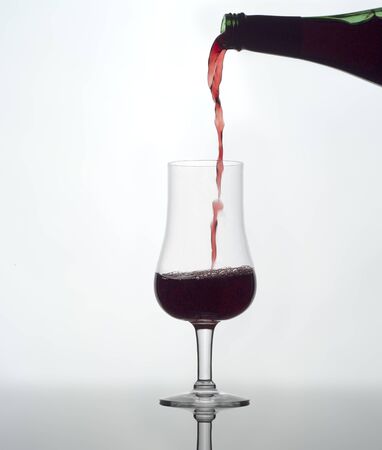 Pouring red wine in a glass on white backgroundの写真素材