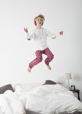 Happy Little Girl with Headphones jumping in bedの写真素材