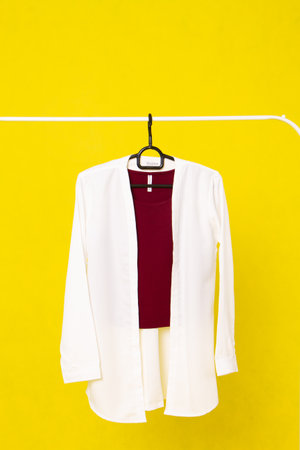 White blouse hanging on a clothes rack on a yellow background.の写真素材