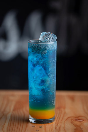 Blue Lagoon mojito. A Mocktail drink which is soda and blue in colour served with ice cubes and fresh orange. Set at cafe on black background and wooden tableの写真素材