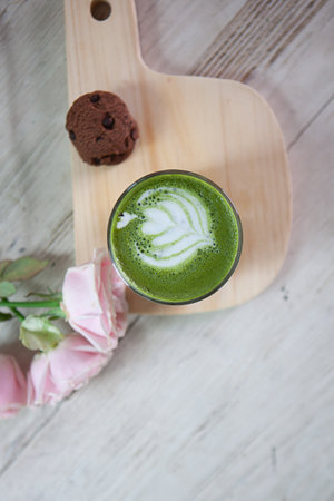Hot Matcha Latte Green Tea with milk foam in glass on wooden board with cookies and flowerの写真素材