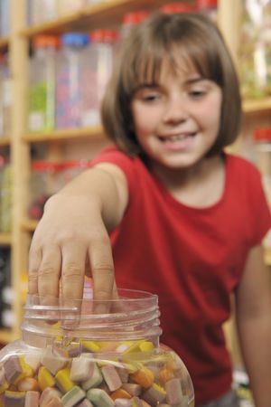 young girl grabbing sweets from a jar in a shopの写真素材