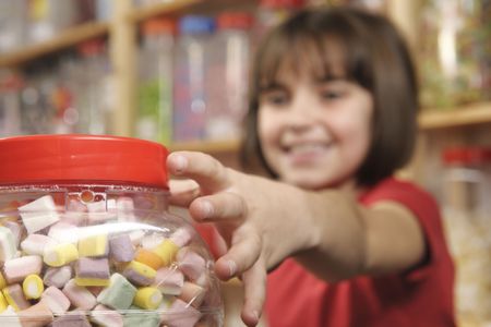 young girl grabbing a jar of sweets in shopの写真素材