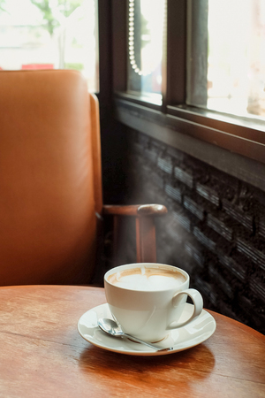 A cup of coffee on the wooden table near window with brown chair and vintage color.の写真素材