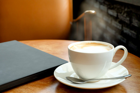 A cup of coffee on the wooden table with black laptop and brown chair. (vintage color)の写真素材