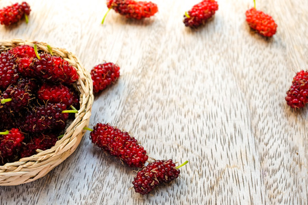 Malberries in small handmade basket on wooden plate (selective focus)の写真素材