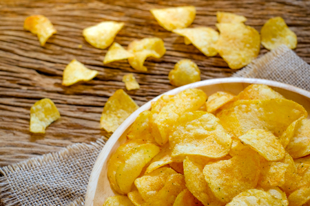 Crispy potato chips with seasoning in plate on sack with wooden background. (top view)の写真素材