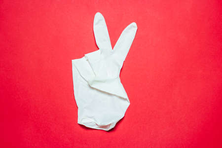 Latex glove showing V sign on red background. Victory over coronavirus (COVID-19) conceptの写真素材