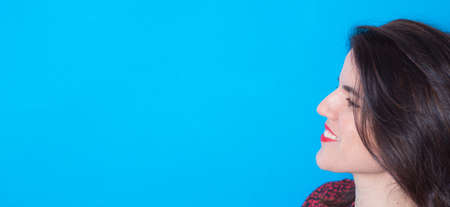 Young smiling woman face profile side view isolated on blue background. Copy space.の写真素材