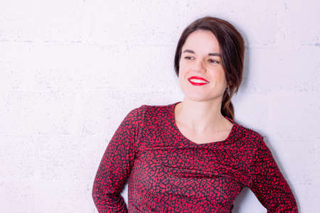Young beautiful woman wearing colorful dress of red or black spots standing over white wall. She is...