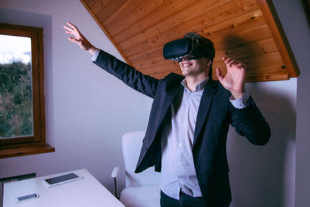 Amazed young man wearing virtual reality headset at home and touching the airの写真素材