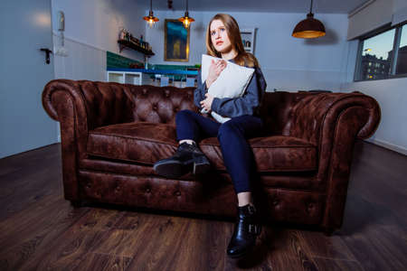 Frontal portrait of a scared young woman alone at home sitting on the couch watching a scary movie on tv.の写真素材