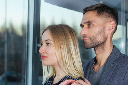 Portrait of a couple of lovers looking through the window of their apartment. They visualize a...