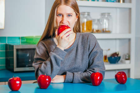 Healthy food concept. Front view of happy young beautiful woman biting a red apple while standing in...