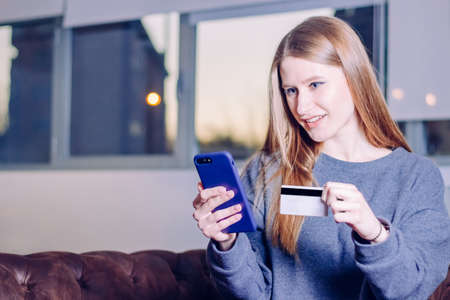 Happy young girl using mobile phone to buy online sitting on the couch at home.
