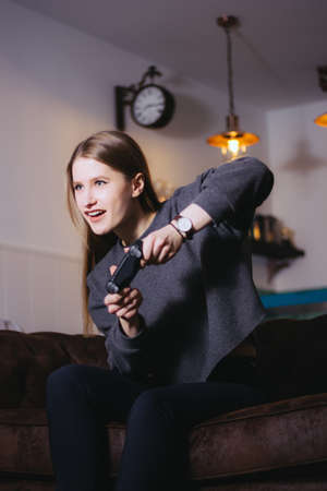 Happy girl enjoying playing video games sitting on sofa at home