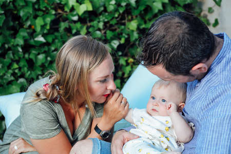 Young mother and father holding their baby daughter with love and affection. Happy family outdoors in the home garden in summerの写真素材