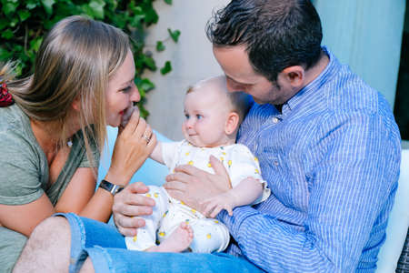 Happy mother and father holding their baby daughter with love and affection outdoors in the home gardenの写真素材