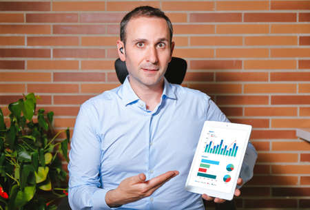 Portrait of young businessman showing data displayed on a tablet screen. Front view. Videoconference conceptの写真素材