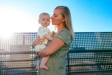 Loving mom holding her baby outdoors. Young mother hugging and kissing her little daughterの写真素材